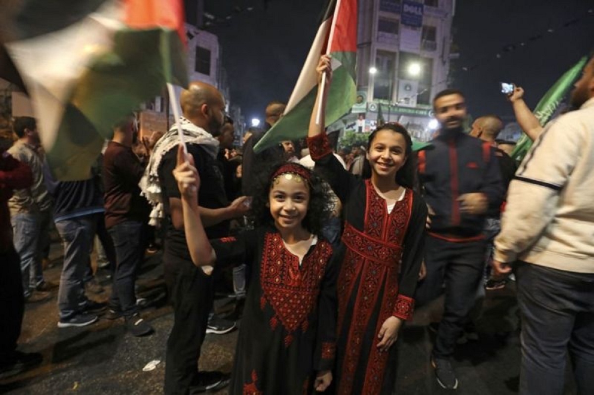 foto : Dua anak perempuan di Kota Ramallah mengibarkan bendera Palestina setelah muncul gencatan senjata antara Israel dan Hamas pada Jumat dini hari 21 Mei 2021 (AFP VIA GETTY IMAGES).