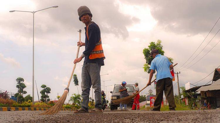 Seorang petugas kebersihan membersihkan cangkang sawit yang berserakan di Jalan Baypas Padang